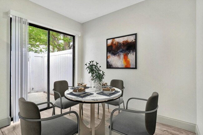 Luminoso comedor con elegante mesa para cuatro personas, decoración artística en las paredes y vista al jardín a través de grandes puertas corredizas. - Temple Crest Townhomes