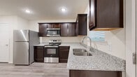 This single-story 2-bedroom, 1-bathroom home offers a thoughtfully designed layout with quality finishes throughout. The kitchen is a standout feature, showcasing rich dark espresso cabinetry, speckled granite countertops, a stainless steel undermount double sink, and a full suite of stainless steel appliances including a refrigerator, electric range with built-in microwave, and dishwasher. Light wood-look flooring runs through the main living areas, complementing the neutral, warm-toned walls. The open living room is generously sized, bathed in recessed lighting, and topped with a ceiling fan for year-round comfort. Both bedrooms are carpeted and feature ceiling fans and windows that allow in natural light, with two closets providing ample storage. The bathroom mirrors the kitchen's design aesthetic with matching dark cabinetry, granite countertops, a large vanity mirror, and a tub/shower combo. A dedicated laundry room with washer and dryer hookups adds everyday convenience. Clean white trim and neutral tones throughout lend the home a fresh, move-in-ready feel.