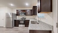 This single-story 2-bedroom, 1-bathroom home offers a thoughtfully designed layout with quality finishes throughout. The kitchen is a standout feature, showcasing rich dark espresso cabinetry, speckled granite countertops, a stainless steel undermount double sink, and a full suite of stainless steel appliances including a refrigerator, electric range with built-in microwave, and dishwasher. Light wood-look flooring runs through the main living areas, complementing the neutral, warm-toned walls. The open living room is generously sized, bathed in recessed lighting, and topped with a ceiling fan for year-round comfort. Both bedrooms are carpeted and feature ceiling fans and windows that allow in natural light, with two closets providing ample storage. The bathroom mirrors the kitchen's design aesthetic with matching dark cabinetry, granite countertops, a large vanity mirror, and a tub/shower combo. A dedicated laundry room with washer and dryer hookups adds everyday convenience. Clean white trim and neutral tones throughout lend the home a fresh, move-in-ready feel.