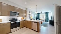 Located at 40445 Portola Ave in Palm Desert, CA, this one-bedroom, one-bathroom residence offers a well-designed layout across a single living floor. The open-concept floor plan seamlessly connects the kitchen and living areas, maximizing the efficient use of space.

The kitchen is a standout feature, outfitted with warm wood cabinetry, a white quartz peninsula with bar seating, stainless steel appliances including a refrigerator, range, microwave, and dishwasher, and a white tile backsplash. Pendant lighting above the peninsula adds a modern touch, while light wood-style flooring runs throughout.

The living area is bright and welcoming, featuring large windows dressed with teal patterned drapes that frame views of mature palm trees outside. A ceiling fan, open wall space for art, and a secondary seating area make the room versatile and comfortable.

The bedroom is a calm retreat with plush carpeting, a ceiling fan, natural light from a window with views, and a dedicated closet. The full bathroom connects conveniently to the bedroom and features warm wood cabinetry, a white quartz vanity, a glass-enclosed shower, and tile flooring. The cohesive design throughout reflects a clean, contemporary aesthetic well-suited for Palm Desert living.