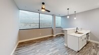 Located at 1230 Elm St in Manchester, NH, this well-designed 2-bedroom, 1-bathroom unit offers a thoughtfully laid-out single-floor living space with contemporary finishes throughout. The open-concept kitchen and dining area serves as the heart of the home, featuring crisp white shaker cabinetry, striking marble-veined quartz countertops, a subway tile backsplash, and a full suite of stainless steel appliances including a refrigerator with ice maker, electric range, microwave, and dishwasher. Elegant pendant lighting and a peninsula with a matte black faucet and sink anchor the space, while large floor-to-ceiling windows flood the living and dining areas with natural light and offer open views of the surrounding cityscape. A modern ceiling fan complements the bright, airy atmosphere of the living area. Durable wood-look plank flooring runs throughout the main living spaces, transitioning to patterned carpet in both bedrooms. The primary bedroom includes a walk-in closet with built-in shelving, while the second bedroom also features a closet. The bathroom is finished with wood-look tile flooring, a full soaking tub and shower combo, and matte black fixtures. Neutral gray walls and clean white trim create a cohesive, modern palette throughout the entire unit.