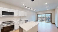 Unit 511 at 304 Persimmon St in Peoria, IL is a thoughtfully designed one-bedroom, one-bathroom residence that makes efficient use of its compact footprint. The open-concept kitchen serves as a central highlight, featuring crisp white shaker cabinetry, light countertops, and a full suite of stainless steel appliances including a refrigerator with ice maker, gas range, built-in microwave, and dishwasher. A center island with a contrasting blue base provides additional prep space and casual seating, while a sleek pendant light fixture adds a modern touch overhead. Recessed lighting and large windows ensure the kitchen and living areas remain bright and inviting. The bedroom is a comfortable, well-proportioned retreat with warm wood-look flooring, neutral walls, a ceiling fan with light, and a generously sized window fitted with blinds that frame views of the surrounding cityscape. A dedicated hallway leads to a closet with built-in hanging rods, offering practical storage solutions. Dark-framed door accents and consistent wood-look flooring throughout the unit tie the design together with a clean, contemporary aesthetic. The overall ambiance is modern and move-in ready, ideal for those seeking comfortable urban living in downtown Peoria.