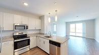 Located at 254 Lynnway Parkway in Lynn, Massachusetts, this single-floor residence offers a thoughtfully designed layout with modern finishes and impressive waterfront views. The open-concept kitchen is a standout feature, showcasing white shaker cabinetry, granite countertops, a peninsula with pendant lighting, and a full suite of stainless steel appliances including a refrigerator, range, microwave, and dishwasher. Warm hardwood-style flooring runs throughout the main living areas, adding a clean, contemporary feel. The spacious living area benefits from large floor-to-ceiling windows that frame serene water views, while track lighting adds a functional and stylish touch. The bedrooms are carpeted for comfort, finished in neutral tones, and include closets for convenient storage. The bathroom is clean and modern, featuring a sliding glass walk-in shower with white tile surround and light tile flooring. Throughout the unit, a soft, neutral color palette and recessed lighting create a bright and welcoming ambiance. The thoughtful open floor plan connects the kitchen and living areas seamlessly, making the space feel airy and well-proportioned — an ideal setting for both everyday living and entertaining.