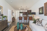 This thoughtfully designed single-floor residence offers a cohesive blend of modern finishes and warm, inviting interiors. Rich, dark hardwood-style flooring flows throughout the main living areas, anchoring the space with a sense of depth and continuity.

The kitchen is a standout feature, showcasing dark espresso cabinetry, granite countertops, and a full suite of stainless steel appliances including a refrigerator, range, and microwave. A peninsula with seating provides a casual dining option beneath stylish pendant lighting, while elevated ceilings lend an open, airy feel.

The living area is bright and welcoming, with large windows dressed in sheer curtains that allow generous natural light. The space comfortably accommodates both a sofa seating arrangement and accent chairs, creating a versatile layout.

Two bedrooms offer a comfortable retreat, each with plush carpeting and windows overlooking the surroundings. The bathrooms are finished with dark cabinetry and granite-topped vanities, with one featuring a tub-shower combination.

A central hallway connects all rooms efficiently, lined with paneled white doors that maintain a clean, consistent aesthetic. Throughout the residence, neutral wall tones and quality finishes create a polished, move-in-ready environment.