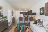 This thoughtfully designed single-floor residence offers a cohesive blend of modern finishes and warm, inviting interiors. Rich, dark hardwood-style flooring flows throughout the main living areas, anchoring the space with a sense of depth and continuity.

The kitchen is a standout feature, showcasing dark espresso cabinetry, granite countertops, and a full suite of stainless steel appliances including a refrigerator, range, and microwave. A peninsula with seating provides a casual dining option beneath stylish pendant lighting, while elevated ceilings lend an open, airy feel.

The living area is bright and welcoming, with large windows dressed in sheer curtains that allow generous natural light. The space comfortably accommodates both a sofa seating arrangement and accent chairs, creating a versatile layout.

Two bedrooms offer a comfortable retreat, each with plush carpeting and windows overlooking the surroundings. The bathrooms are finished with dark cabinetry and granite-topped vanities, with one featuring a tub-shower combination.

A central hallway connects all rooms efficiently, lined with paneled white doors that maintain a clean, consistent aesthetic. Throughout the residence, neutral wall tones and quality finishes create a polished, move-in-ready environment.