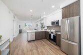 Located at 800 S Western Ave in Los Angeles, this well-appointed one-bedroom, one-bathroom unit offers a thoughtfully designed open-concept layout. The combined kitchen and living area forms the heart of the space, featuring warm hardwood-style flooring, recessed lighting, and expansive windows that frame sweeping city skyline views and flood the interior with natural light. The modern kitchen is outfitted with stainless steel appliances — including a full-size refrigerator, range, microwave, and dishwasher — complemented by two-tone cabinetry in white and rich dark wood, a tile backsplash, and a peninsula with pendant lighting that doubles as a breakfast bar. The living area provides a comfortable retreat with generous wall space and large windows overlooking the Los Angeles cityscape. The bedroom is a bright, serene space highlighted by a large picture window with continued city views and light neutral walls. Two closets, including a spacious walk-in with built-in shelving and hanging rods, provide ample storage. The full bathroom features large-format marble-look tile flooring, a dark wood vanity with a backlit mirror, and a full soaking tub with shower.