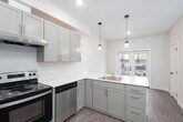 This contemporary apartment spans three floors, offering a blend of style and functionality. The heart of the home is a well-appointed kitchen, showcasing light gray cabinetry, quartz countertops, and stainless steel appliances. The L-shaped layout maximizes space efficiency, while pendant lights add a touch of elegance.

The living areas boast wood-look flooring, creating a warm and inviting atmosphere. Large windows flood the rooms with natural light, offering urban views and a sense of openness. The bathroom continues the modern aesthetic with a clean white palette, featuring a vanity with ample storage and a shower/tub combination.

Each floor is thoughtfully designed, with the upper levels likely housing bedrooms and additional living spaces. The apartment's open concept design promotes a seamless flow between areas, ideal for both everyday living and entertaining. Recessed lighting throughout ensures a bright, welcoming environment at any time of day.

The property's attention to detail is evident in its neutral color scheme, allowing residents to easily personalize their space. With its combination of style, comfort, and urban sophistication, this three-floor apartment offers a desirable living experience in a contemporary setting.
