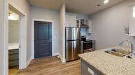 Located at 256 Apala Circle in Lynchburg, Virginia, this single-floor unit showcases a clean, contemporary design with a cohesive color palette of soft grays and muted blues carried throughout the space. Durable wood-look luxury vinyl plank flooring runs continuously across all rooms, providing both visual warmth and easy maintenance.

The kitchen serves as a functional centerpiece, featuring stainless steel appliances including a refrigerator, range with electric cooktop, built-in microwave, and dishwasher. White upper cabinetry with glass-front accents is paired with gray lower cabinets, and granite-look countertops extend to a peninsula with pendant lighting overhead. A white subway tile backsplash and wall-mounted range hood complete the polished look.

The open living and dining area flows naturally from the kitchen, with a bold accent wall adding depth and a doorway leading to additional rooms. The living space offers ample room and benefits from recessed lighting and large windows dressed with white horizontal blinds, inviting generous natural light.

The bedrooms maintain the same light gray walls and vinyl flooring, each equipped with ceiling fans and windows. The bathroom features a soaking tub and shower combination with white tile surround and a curved chrome curtain rod, offering a clean and functional design.