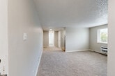 Located at 1054 S Dahlia St in Glendale, Colorado, this one-bedroom, one-bathroom residence offers a practical and efficient single-floor layout. The living room is open and spacious, featuring soft wall-to-wall carpeting, neutral gray walls, and a textured ceiling that carries throughout the home. Baseboard heating runs along the perimeter of the rooms, ensuring consistent warmth. The space flows through a connecting hallway that leads to the bedroom and bathroom.

The bedroom is a comfortable, well-proportioned room with plush carpeting, a window fitted with horizontal blinds that allows natural light and outdoor greenery views, a wall-mounted HVAC unit, and a closet for convenient storage. The textured ceiling and neutral tones keep the room feeling calm and cohesive.

The bathroom is clean and functional, featuring a full soaking tub with a tiled surround and a window above that brings in natural light. The all-white palette creates a bright, crisp atmosphere.

The kitchen area, visible in the floor plan, is efficiently laid out and connects to the living space. Throughout the residence, the consistent use of neutral tones, soft carpeting, and clean white trim creates a cohesive and understated aesthetic well-suited for comfortable everyday living.