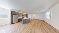 This contemporary single-floor residence offers a thoughtfully designed open-concept layout that seamlessly connects the kitchen, dining, and living areas. Light wood plank flooring flows throughout the space, creating a warm and cohesive aesthetic.

The kitchen is a standout feature, showcasing dark wood cabinetry, a white subway tile backsplash, and crisp white quartz countertops. A central island with an integrated sink and a sleek pull-down faucet provides additional prep space and a natural gathering point. Stainless steel appliances, including a gas range, over-the-range microwave, and full-size refrigerator, complete the modern setup. A dedicated laundry closet with a stacked washer and dryer unit is conveniently located nearby.

The expansive living area is bathed in natural light from multiple windows with blinds, offering views of the surrounding neighborhood. Recessed lighting and track-style fixtures provide well-distributed illumination throughout.

The bathroom is finished with large-format tile on the shower and tub surround, complemented by a floating vanity with a white quartz countertop and a wide mirror. Bedrooms are bright and versatile, with one featuring a generous walk-in closet with built-in shelving and hanging rods. The overall design is clean, modern, and move-in ready.