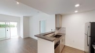 This single-level 1-bedroom, 1-bathroom residence is thoughtfully designed to maximize both functionality and style. The open-concept layout creates a seamless flow between the kitchen and living area, making the space feel airy and connected. The kitchen serves as a central feature, highlighted by a peninsula with a dark stone countertop that provides ample prep space and casual seating opportunities. Light wood cabinetry with clean-lined hardware adds warmth, while a mosaic tile backsplash introduces a subtle decorative accent. An undermount sink and built-in appliances complete the well-appointed kitchen setup. The living area extends naturally from the kitchen, offering a clean, open canvas with smooth white walls and warm wood-toned flooring that runs throughout the unit. A frosted glass door adds a modern touch while allowing light to pass between spaces. The overall palette of neutral tones — whites, warm woods, and dark stone accents — creates a contemporary and cohesive aesthetic. This residence is designed with everyday comfort in mind, offering a practical and polished environment suited to a modern lifestyle.
