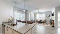 Located at 1871 Ashley River Rd in Charleston, SC, this well-appointed one-bedroom, two-bathroom residence offers a thoughtfully designed single-floor layout that maximizes both comfort and functionality. Light wood-style flooring flows throughout the main living areas, complementing the neutral gray and white color palette that gives the space a clean, modern feel.

The open-concept kitchen is a standout feature, boasting a large island with seating for multiple bar stools, pendant lighting, light wood cabinetry, stainless steel appliances including a full-size refrigerator, and ample counter space. The kitchen opens directly into the dining and living areas, making it ideal for entertaining.

The living room is bright and welcoming, with multiple windows dressed in sheer white curtains and wood-slat blinds that invite generous natural light. A ceiling fan adds to the comfort of the space, which also provides direct access to the outdoors via a side door.

The private bedroom features soft carpeting, a ceiling fan, and a well-sized window with natural light. An adjacent walk-in closet with wire shelving provides practical storage. The two bathrooms include a vanity with light wood cabinetry and white countertops.

A dedicated in-unit laundry room with full-size washer and dryer completes this efficiently designed Charleston residence.
