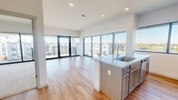 This well-appointed 3-bedroom, 2-bathroom residence is situated on an upper floor and offers a bright, contemporary living experience throughout. The open-concept layout seamlessly connects the kitchen and living room, both of which are bathed in abundant natural light through expansive floor-to-ceiling windows that frame sweeping views of the surrounding neighborhood and skyline. The kitchen features granite countertops, a central island with an undermount sink, and stainless steel appliances, including a dishwasher. Light hardwood flooring runs throughout the main living areas, complementing the clean white walls and recessed lighting overhead. The living room opens directly onto a private balcony through large glass doors, extending the living space outdoors. A long, light-filled hallway connects the common areas to the private quarters, where three carpeted bedrooms offer comfortable retreats. The generously sized primary bedroom includes an en-suite bathroom complete with a glass-enclosed shower, granite vanity, and a walk-in closet. The secondary bedrooms are well-proportioned and share access to a second full bathroom. A dedicated laundry room with a full-size washer and dryer adds everyday convenience, rounding out this thoughtfully designed and move-in-ready residence.