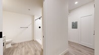 This efficiently designed one-bedroom, one-bathroom unit offers a thoughtfully organized single-floor layout. Light wood-look luxury vinyl plank flooring and bright white walls are consistent throughout, creating a clean, cohesive aesthetic.

The galley-style kitchen is a standout feature, equipped with stainless steel appliances including an electric range, built-in microwave, dishwasher, and refrigerator. Sage-toned cabinetry with matte black hardware pairs with white quartz countertops and a matte black faucet at the undermount sink, delivering a modern, updated look. Recessed lighting and a window at the end of the kitchen allow natural light to filter in.

The combined kitchen and living area flows into a hallway connecting the remaining rooms. The bedroom is a compact, well-proportioned space featuring an overhead closet rod and upper windows that bring in natural light and views of surrounding greenery.

The bathroom includes a walk-in shower with matte black fixtures and a towel bar, finished in a clean white palette with wood-look flooring. A dedicated laundry room houses an LG combination washer unit with overhead wire shelving, adding practical convenience. An electrical panel is also accessible from the hallway area.