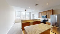 Situated in the heart of downtown Cincinnati on Main Street, this single-floor residence offers a well-designed open layout with distinct living, kitchen, and bedroom areas. The kitchen serves as a central highlight, featuring rich warm-toned cabinetry, expansive granite countertops across dual islands, stainless steel appliances including an electric range and over-the-range microwave, a built-in dishwasher, and a white subway tile backsplash with decorative mosaic accents. A double sink with a gooseneck faucet anchors the kitchen island, which flows seamlessly into the main living area.

The living space is generously proportioned with plush carpeting and a ceiling fan, bathed in natural light from a large bank of multi-pane windows that frame impressive views of the Cincinnati skyline. A separate bedroom also benefits from large city-facing windows and ceiling fan. Storage is well-addressed with a walk-in closet outfitted with multi-tiered wire shelving and hanging rods.

Two bathrooms serve the unit: one features a tub/shower combination with dark oil-rubbed bronze fixtures and tile flooring, while the other includes a glass-enclosed walk-in shower with matching dark hardware. The overall ambiance is bright, clean, and urban.