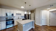 The Buchanan is a well-appointed 2-bedroom, 2-bathroom residence located in Cypress, TX, offering a thoughtfully designed single-floor layout. Rich, dark hardwood-style flooring flows consistently throughout the entire home, creating a cohesive and polished aesthetic.

The open-concept kitchen is a standout feature, showcasing white shaker cabinetry, a classic subway tile backsplash, granite countertops, and a full suite of stainless steel appliances including a refrigerator, range, microwave, and dishwasher. A central granite-topped island with pendant lighting above serves as an ideal prep and gathering space, seamlessly connecting the kitchen to the living area.

The spacious living area is illuminated by a ceiling fan with integrated lighting, lending comfort and airflow year-round. Each bedroom is generously sized, also featuring ceiling fans, and is supported by ample closet storage with built-in wire shelving systems.

The two bathrooms are finished with white vanities, large mirrors with overhead lighting, and white countertops. The primary bathroom includes a soaking tub with tile surround and a dual-sink vanity offering extensive storage. A dedicated in-unit laundry room houses a full-size washer and dryer, adding everyday convenience to this well-rounded residence.