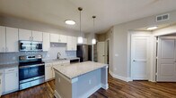 The Buchanan is a well-appointed 2-bedroom, 2-bathroom residence located in Cypress, TX, offering a thoughtfully designed single-floor layout. Rich, dark hardwood-style flooring flows consistently throughout the entire home, creating a cohesive and polished aesthetic.

The open-concept kitchen is a standout feature, showcasing white shaker cabinetry, a classic subway tile backsplash, granite countertops, and a full suite of stainless steel appliances including a refrigerator, range, microwave, and dishwasher. A central granite-topped island with pendant lighting above serves as an ideal prep and gathering space, seamlessly connecting the kitchen to the living area.

The spacious living area is illuminated by a ceiling fan with integrated lighting, lending comfort and airflow year-round. Each bedroom is generously sized, also featuring ceiling fans, and is supported by ample closet storage with built-in wire shelving systems.

The two bathrooms are finished with white vanities, large mirrors with overhead lighting, and white countertops. The primary bathroom includes a soaking tub with tile surround and a dual-sink vanity offering extensive storage. A dedicated in-unit laundry room houses a full-size washer and dryer, adding everyday convenience to this well-rounded residence.