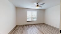 This single-floor unit offers a clean, contemporary design highlighted by light wood-style luxury vinyl plank flooring that runs consistently throughout the space, creating a cohesive and polished aesthetic. The galley-style kitchen is well-equipped, featuring dark espresso cabinetry with brushed nickel hardware, light granite-style countertops, and a full suite of stainless steel appliances including an electric range, dishwasher, built-in microwave, and refrigerator. A stacked washer and dryer unit is conveniently housed just off the kitchen, adding practical in-unit laundry access.

The living and bedroom areas are spacious and open, dressed in warm neutral tones with clean white trim and baseboards. Bedrooms are equipped with ceiling fans with integrated lighting and windows fitted with horizontal blinds, allowing for natural light control. The overall layout, visible in the 3D scan, reflects an efficient and functional floor plan.

The bathroom continues the design language of the rest of the unit, with matching dark cabinetry, a granite-style vanity countertop, a tall storage tower, a large mirror, and a full tub-shower combination with built-in shelving. Light flooring and bright white fixtures keep the space feeling fresh and clean throughout.