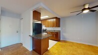 This single-floor residence offers a functional and cohesive layout with consistent design elements throughout. The kitchen is a standout area, outfitted with rich warm-toned wood cabinetry, dark granite countertops, and stainless steel appliances including a gas range and refrigerator. A peninsula with a matching granite surface extends into the adjacent living space, creating a natural transition between the kitchen and the main living area. The kitchen floor features light ceramic tile, while the rest of the unit showcases polished parquet wood flooring that adds warmth and character throughout.

The open living area is generously proportioned and filled with natural light from a large picture window fitted with vertical blinds, offering a pleasant view of surrounding greenery. A ceiling fan enhances comfort in this main gathering space. The bedroom is a well-sized room with gleaming parquet floors, soft neutral walls, and a built-in open closet with shelving, providing ample storage. An additional door leads to a hallway, connecting the room to the rest of the unit.

The bathroom is cleanly finished with tile flooring, a granite-topped vanity with wood cabinetry, and a full-size soaking tub with an overhead shower. The space presents a cohesive, practical interior with quality finishes throughout.