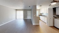 This single-floor, 1-bedroom, 1-bathroom unit offers a practical and comfortable layout with neutral grey and beige tones throughout. The living area is a standout space, featuring warm wood-look vinyl flooring, a textured ceiling, and a white-mantled fireplace with a classic surround, adding character and warmth. A sliding glass door and additional window bring in natural light and provide access to the exterior. The galley-style kitchen is efficiently designed with white cabinetry, dark countertops, a stainless steel sink, and a full suite of appliances including a gas range, refrigerator, and dishwasher. A louvered bi-fold door conceals a dedicated in-unit laundry area with a stacked washer and dryer. The bedroom is carpeted and features generous closet space with dual reach-in closets, a window with blinds for natural light, and direct access to adjacent areas. The bathroom includes a clean, white tub and shower combination with chrome fixtures. Overall, the unit presents a clean, move-in-ready aesthetic with consistent finishes and practical storage throughout.