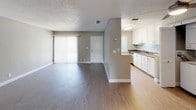 This single-floor, 1-bedroom, 1-bathroom unit offers a practical and comfortable layout with neutral grey and beige tones throughout. The living area is a standout space, featuring warm wood-look vinyl flooring, a textured ceiling, and a white-mantled fireplace with a classic surround, adding character and warmth. A sliding glass door and additional window bring in natural light and provide access to the exterior. The galley-style kitchen is efficiently designed with white cabinetry, dark countertops, a stainless steel sink, and a full suite of appliances including a gas range, refrigerator, and dishwasher. A louvered bi-fold door conceals a dedicated in-unit laundry area with a stacked washer and dryer. The bedroom is carpeted and features generous closet space with dual reach-in closets, a window with blinds for natural light, and direct access to adjacent areas. The bathroom includes a clean, white tub and shower combination with chrome fixtures. Overall, the unit presents a clean, move-in-ready aesthetic with consistent finishes and practical storage throughout.