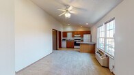 Located at 2419 W Bradley Ave in Champaign, Illinois, this single-floor unit offers a practical and functional layout designed to maximize usable space. The open-concept living and kitchen area is a defining feature, characterized by vaulted ceilings that lend a sense of spaciousness and airiness. A ceiling fan with integrated lighting is centrally mounted, providing both ventilation and ambient illumination. Natural light enters through a sizable window, brightening the carpeted living area.

The kitchen is well-equipped with warm-toned oak cabinetry extending to the upper walls, offering generous storage. Appliances include a range with an overhead exhaust, a refrigerator, a dishwasher, and a microwave. A peninsula counter separates the kitchen from the living space, adding both prep area and a visual boundary. The kitchen floor is finished in light vinyl tile.

Additional rooms include a carpeted bedroom-sized space with its own window, ceiling fan, and a baseboard heating unit, along with a separate area housing an electrical panel. The full bathroom features a single-sink oak vanity with a large mirror, a tub-shower combination, and light tile flooring. Warm wood-toned doors are consistent throughout, contributing to a cohesive interior aesthetic.