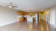 This single-floor space offers a well-organized, open layout designed for comfortable everyday living. Warm wood-look flooring flows consistently throughout, unifying each area while contributing to a clean, contemporary aesthetic. Neutral gray and beige wall tones complement the overall palette and provide a versatile backdrop.

The kitchen serves as a functional centerpiece, outfitted with natural wood cabinetry, light countertops, and a full suite of stainless steel appliances including a range, microwave, dishwasher, and refrigerator. A central island with pendant lighting above adds both prep space and visual interest, while the open-concept design allows the kitchen to connect seamlessly with the adjacent living area. A wet bar with additional cabinetry and a window adds a practical secondary amenity to the living space.

The living area is generously proportioned, featuring recessed lighting and clear sightlines to the kitchen pass-through. Bedrooms are served by a spacious walk-in closet equipped with wire shelving on multiple levels, maximizing storage capacity. The bathroom includes a walk-in shower with a white surround and continues the consistent flooring found throughout the unit. White trim and baseboards provide crisp definition to each room.