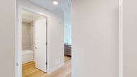 This well-appointed 3-bedroom, 2-bathroom residence is thoughtfully designed across a single floor, offering a clean, modern aesthetic throughout. Light hardwood flooring flows consistently through every room, complemented by crisp white walls and recessed lighting that create a bright, airy atmosphere.

The kitchen features a peninsula with a sleek quartz countertop, stainless steel appliances including a refrigerator, microwave, and dishwasher, and a combination of white upper cabinetry and warm wood-toned lower cabinets. It opens conveniently toward the living area for an efficient, connected layout.

The living room is a standout space, bathed in natural light from oversized floor-to-ceiling windows that offer open views of the surrounding urban and treetop scenery. A balcony extends the living space outdoors. The three bedrooms are comfortably proportioned, with the primary bedroom featuring large windows framing greenery views, a sliding door, and a baseboard heating system. The additional bedrooms are bright and well-sized.

The bathrooms are finished with large-format tile surrounds in the tub/shower, warm wood-grain vanity cabinetry, quartz countertops, and undermount sinks. A hallway connects the rooms efficiently, with in-unit laundry also present. The overall ambiance is clean, contemporary, and move-in ready.