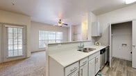 This single-floor, 1-bedroom, 1-bathroom residence is designed for comfortable, efficient living. The open-concept layout connects the kitchen and living room seamlessly, with a peninsula counter serving as both a functional workspace and a visual divider between the two areas. The kitchen features white cabinetry with modern hardware, light stone countertops, a mosaic tile backsplash, wood-look flooring, and a full suite of stainless steel appliances including a refrigerator, range, microwave, and dishwasher. A separate pantry provides generous storage. The living room is carpeted and bright, benefiting from large windows with blinds and a ceiling fan with integrated lighting. Built-in shelving adds a functional architectural touch to the living space. The bedroom is generously sized, also carpeted, and includes a ceiling fan, a sliding glass door for natural light, and direct access to both a walk-in closet and an en-suite bathroom. The bathroom is finished with tile flooring and features a full tub-shower combination. Three closets throughout the residence ensure abundant storage. The overall aesthetic is clean and neutral, with a bright, airy ambiance throughout.