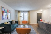This two-story residence in Atlanta, GA (30339) showcases a cohesive mid-century modern aesthetic throughout its thoughtfully designed layout. The upper level centers around a welcoming living area with wood-look flooring, where a tufted teal sofa, mustard accent chairs, and bold colorful wall art create a vibrant yet curated atmosphere. A dedicated workspace with a compact desk integrates seamlessly into the living space, offering functional versatility. A staircase with a classic white baluster railing connects both floors.

The kitchen features white shaker cabinetry, granite-style countertops, stainless steel appliances, and wood-look flooring, providing a clean and functional cooking environment. The bedrooms are finished with plush carpeting and offer a calm, neutral palette, each accommodating comfortable furnishings with ample space. Closet access and natural light from windows contribute to the livability of each room.

The bathrooms are well-appointed, with one featuring white cabinetry, a granite-topped vanity, wood flooring, and modern lighting, while another includes a tub-shower combination with stylish tiled surrounds. Throughout both levels, the space maintains a consistent, design-forward identity with textured ceilings and warm, inviting tones.