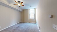 Located in Cincinnati's 45202 zip code, this single-floor residence at 207 Eighth St E offers a thoughtfully designed layout with a neutral, move-in-ready aesthetic throughout. The kitchen serves as a functional centerpiece, outfitted with rich wood cabinetry, granite countertops, a subway tile backsplash, and a full suite of stainless steel appliances including a French door refrigerator, gas range with microwave, and a double-basin sink. A central island provides additional prep and gathering space, while tile flooring adds durability underfoot. The living and sleeping areas feature plush wall-to-wall carpeting in a soft gray tone, complemented by warm beige walls and clean white trim. Ceiling fans are present in the main carpeted rooms, promoting airflow and comfort. Natural light enters through tall, double-hung windows that frame views of the surrounding brick urban streetscape, lending an airy quality to the interior. The bathroom is finished with light tile flooring, a warm wood vanity with ample cabinetry and drawers, a white countertop, and a framed mirror with overhead lighting. The overall ambiance is clean, understated, and well-maintained, offering a comfortable urban living environment in the heart of Cincinnati.