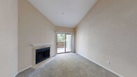 This single-floor residence offers a thoughtfully designed layout with a warm, neutral color palette throughout. The living room immediately impresses with its soaring vaulted ceilings that lend an airy, open feel to the space. A tile-surround fireplace with a clean white mantle serves as a striking focal point, while a sliding glass door opens directly onto a private balcony overlooking lush greenery, filling the room with natural light. The carpeted flooring adds warmth and comfort underfoot.

The kitchen is outfitted with rich dark-wood cabinetry featuring sleek hardware, light stone countertops, and a stainless steel sink. A built-in dishwasher and a tall pantry cabinet provide ample storage and functionality. Wood-look flooring ties the space together with a modern touch.

The bedrooms are generously sized, each featuring plush carpet, ceiling fans with light fixtures, and large windows or sliding doors that invite natural light and outdoor views. The bright, neutral walls create a versatile canvas throughout.

The bathroom features a stone-topped vanity with an undermount sink, a wide mirror, and a tiled shower enclosure, offering a clean and contemporary finish. Overall, this residence combines practical design with comfortable, light-filled living spaces.