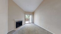 This single-floor residence offers a thoughtfully designed layout with a warm, neutral color palette throughout. The living room immediately impresses with its soaring vaulted ceilings that lend an airy, open feel to the space. A tile-surround fireplace with a clean white mantle serves as a striking focal point, while a sliding glass door opens directly onto a private balcony overlooking lush greenery, filling the room with natural light. The carpeted flooring adds warmth and comfort underfoot.

The kitchen is outfitted with rich dark-wood cabinetry featuring sleek hardware, light stone countertops, and a stainless steel sink. A built-in dishwasher and a tall pantry cabinet provide ample storage and functionality. Wood-look flooring ties the space together with a modern touch.

The bedrooms are generously sized, each featuring plush carpet, ceiling fans with light fixtures, and large windows or sliding doors that invite natural light and outdoor views. The bright, neutral walls create a versatile canvas throughout.

The bathroom features a stone-topped vanity with an undermount sink, a wide mirror, and a tiled shower enclosure, offering a clean and contemporary finish. Overall, this residence combines practical design with comfortable, light-filled living spaces.