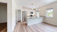 Located at 1471 US-9 in Halfmoon, NY, this well-appointed 2-bedroom, 1-bathroom residence offers a clean, modern aesthetic across a thoughtfully designed single-floor layout. The open-concept kitchen and living area serves as the heart of the home, showcasing crisp white shaker cabinetry, striking granite countertops, and a suite of stainless steel appliances including a refrigerator, range, and microwave. A large center island with an undermount sink and stylish pendant lighting above makes the kitchen both functional and visually appealing. Light-toned hardwood flooring flows seamlessly throughout the main living areas, enhancing the bright, airy ambiance. The spacious living room features recessed lighting and a warm wood-toned entry door. Both bedrooms are generously sized, carpeted for comfort, and filled with natural light from large windows overlooking lush greenery. The primary bedroom includes a dedicated walk-in closet with built-in wire shelving. The full bathroom is finished with a grey shaker-style vanity, granite countertop, undermount sink, and a modern brushed nickel light fixture, all complemented by hardwood flooring. The overall design is fresh, cohesive, and move-in ready.