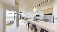 This contemporary urban residence offers a thoughtfully designed single-floor layout with 2 bedrooms and 3 bathrooms. The open-concept living area is anchored by dramatic exposed concrete ceilings and large-format, black-framed floor-to-ceiling windows that flood the space with natural light and frame stunning city and hillside views. A private balcony is accessible directly from the living room, extending the living space outdoors. The kitchen features sleek cabinetry with warm wood accents, a spacious waterfall-edge island with bar seating, and stainless steel appliances, flowing seamlessly into the living area. Light wide-plank hardwood flooring runs throughout, complementing the industrial-modern aesthetic. The entryway features a striking exposed concrete accent wall, setting an artistic tone. Both bedrooms are serene retreats; the primary bedroom boasts floor-to-ceiling windows with outdoor views and a concrete feature wall, while the second bedroom offers a tall, narrow window detail and access to an adjacent bath. Three clean, well-appointed bathrooms include tiled tub-shower combinations. A hallway laundry nook with an in-unit washer adds everyday convenience. Track lighting and recessed fixtures complete the refined industrial character of this well-appointed residence.