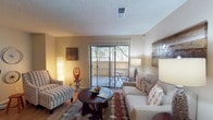 This single-story, one-bedroom, one-bathroom residence offers a thoughtfully organized layout that maximizes its compact footprint. The living room serves as the heart of the unit, featuring wood-style flooring, a textured ceiling, and a full-width sliding glass door fitted with vertical blinds that opens onto a private balcony overlooking greenery. Natural light flows freely into the space, creating a bright and welcoming atmosphere.

The galley-style kitchen runs along a narrow corridor and is equipped with black appliances, including a refrigerator, electric range, and dishwasher. Warm wood cabinetry lines both sides of the kitchen, complemented by granite-style countertops and a double basin sink, providing ample storage and prep space.

The bedroom is carpeted and comfortably sized, featuring a ceiling fan with light fixture and a window that allows natural light to filter in. The room offers sufficient space for a full furniture arrangement.

The bathroom features wood-style flooring extending through a hallway-style layout, with a vanity topped by granite-style counters, warm wood cabinetry with storage drawers, a framed mirror, and a separate tub-shower combination tucked at the end of the corridor.