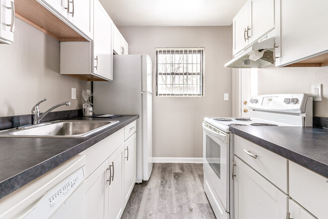 Kitchen with dishwasher, white cabinetry, refrigerator, stove/oven, faux wood flooring, and faux mar - Chartwell Townhouse Apartments