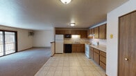 This single-floor residential unit offers a practical and functional layout designed for comfortable everyday living. The open-concept kitchen and living area form the heart of the space, with the kitchen featuring warm oak cabinetry, light-toned laminate countertops, and a full suite of appliances including a white refrigerator, electric range with overhead ventilation, built-in microwave, black dishwasher, and a double stainless steel sink. Light tile flooring runs through the kitchen, transitioning to plush wall-to-wall carpeting in the living area. The living space is generously sized, offering room for multiple furniture arrangements, and includes a wall-mounted air conditioning unit and a sliding glass door that opens to a private balcony. Baseboard heating is present throughout the unit, ensuring consistent warmth. Two carpeted bedrooms are each equipped with windows that let in natural light and are served by baseboard heaters. The full bathroom includes a single-sink vanity with oak cabinetry, a large wall mirror, a tub-shower combination, and tile flooring. The overall design is straightforward and functional, with warm wood tones and neutral walls creating a cohesive, understated aesthetic throughout.