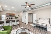 This single-floor residence offers a thoughtfully designed open layout finished with warm wood-look flooring throughout. The living area is bright and inviting, featuring large windows with horizontal blinds that allow generous natural light to fill the space, complemented by a glass-panel door opening directly to an outdoor patio. The kitchen is well-equipped with stainless steel appliances—including a refrigerator, electric range, microwave, and dishwasher—set against granite-look countertops and rich dark wood cabinetry with a classic tile backsplash. An exposed industrial-style ductwork detail adds a contemporary architectural accent overhead. The entryway is open and functional, connecting seamlessly to both the kitchen and main living spaces. The bathroom continues the cohesive design with dark wood vanity cabinetry, granite-look countertops, wood-look flooring, and a narrow window that brings in additional natural light while maintaining privacy. An electrical panel is discreetly integrated into the unit. Throughout the residence, neutral wall tones, consistent flooring, and clean lines create a modern, comfortable ambiance well-suited for everyday living.