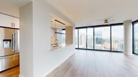 Located at 903 Peachtree St NE in the heart of Atlanta, this modern high-rise residence delivers a sleek, contemporary living experience with exceptional city and treetop views. The open-concept living and dining area is anchored by expansive floor-to-ceiling windows that flood the space with natural light while framing sweeping panoramic views of the Atlanta skyline and surrounding landscape. Light-toned hardwood flooring runs throughout, enhancing the bright, airy ambiance.

The galley-style kitchen is thoughtfully designed with white upper cabinetry, warm wood lower cabinetry, light quartz countertops, a classic subway tile backsplash, stainless steel appliances including a range with hood, and a wine refrigerator. A pass-through window connects the kitchen to the living area, maintaining the open flow of the space.

The primary bathroom is elegantly appointed with large-format tile flooring, a glass-enclosed shower featuring herringbone-patterned tile walls, a floating wood vanity with an undermount sink, and modern black hardware accents. A secondary bathroom provides clean, minimalist finishes with tile flooring. Additional highlights include a walk-in closet with built-in shelving, recessed lighting throughout, and ceiling fans in the main living areas.