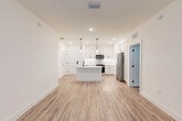 Located at 45 NE Sixth Ave in Delray Beach, Florida, this well-designed 2-bedroom, 3-bathroom residence offers a clean, contemporary aesthetic across a single floor. The open-concept layout seamlessly connects the kitchen and living area, creating a bright and functional shared space. The kitchen is a standout feature, showcasing white shaker cabinetry, quartz countertops, stainless steel appliances including a French door refrigerator and microwave, and a central island with an undermount sink, matte black faucet, and dual pendant lighting overhead — all set against recessed lighting and crisp white walls. Wood-look luxury vinyl flooring runs throughout the home, lending warmth and continuity to every room. The living area benefits from natural light through large windows fitted with horizontal blinds. Both bedrooms are well-proportioned, each with ceiling fans, natural light, and neutral tones. The primary bedroom offers a comfortable footprint with direct access to dedicated closet space featuring built-in wire shelving systems. The three bathrooms are finished with modern fixtures, including a tiled tub-shower combination with matte black hardware. Two closets provide ample storage throughout the home.