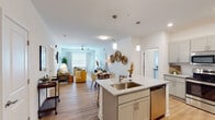 Located at Old Salem Road in Kernersville, NC, this single-floor residence offers a thoughtfully designed open-concept layout with modern finishes. The kitchen serves as a central hub, showcasing gray shaker-style cabinetry, granite-look countertops, a subway tile backsplash, stainless steel appliances including a refrigerator, range, and microwave, and a large center island with a built-in sink and pendant lighting overhead. The kitchen flows seamlessly into a bright, open living and dining area featuring light hardwood-style flooring, a ceiling fan, and large windows that allow generous natural light to fill the space. The living area offers a relaxed, contemporary ambiance with clean white walls and ample room for comfortable furnishings. The bedrooms are carpeted for comfort, each equipped with ceiling fans and windows with blinds and drapes providing privacy and light control. The primary bathroom features a dual-sink vanity with granite-look countertops and gray cabinetry, while the secondary bathroom includes a single vanity and a full shower-tub combo. Light tile flooring and white finishes give both bathrooms a clean, polished look. Throughout the residence, consistent use of gray cabinetry, neutral tones, and modern hardware creates a cohesive and contemporary aesthetic.