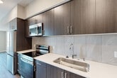 Located at 201 North La Brea Avenue in Inglewood, CA, this thoughtfully designed one-bedroom, one-bathroom unit offers a modern living experience with quality finishes throughout. The open layout encompasses a kitchen, living areas, a well-sized bedroom, and a full bathroom, all connected by warm wood-style plank flooring that flows seamlessly from room to room.

The contemporary kitchen is a standout feature, showcasing rich dark-toned cabinetry that extends to the ceiling for ample storage, crisp white quartz countertops, a marble-style tile backsplash, and a full suite of stainless steel appliances including a range, built-in microwave, dishwasher, and refrigerator. A deep single-basin sink with a modern pull-down faucet completes the space.

The living areas are bathed in natural light through large windows that frame expansive city views, offering a bright and airy atmosphere. The bedroom is generously proportioned, featuring large windows that continue the urban panorama and provide plentiful daylight.

The bathroom is clean and functional, with a dark wood-finish vanity, white countertop, a large wall mirror, tiled shower, and accessibility-friendly grab bars. Neutral warm-toned walls throughout the unit create a cohesive, inviting ambiance well-suited for modern urban living.