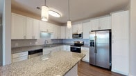 Located at 6701 Fox Rd in Raleigh, NC, this single-floor residence offers a thoughtfully designed layout with contemporary finishes throughout. The kitchen is a standout feature, boasting white shaker-style cabinetry, granite countertops, a subway tile backsplash, a large center island, and a full suite of stainless steel appliances including a French door refrigerator, electric range, microwave, and dishwasher. Pendant lighting adds a polished touch above the island. Durable wood-look flooring runs through the main living and kitchen areas, while plush carpet adds comfort to the bedrooms. The living area is bright and open, benefiting from multiple windows that invite natural light and offer views of the surrounding neighborhood. A ceiling fan enhances comfort in the main living space. Bedrooms include generous closet space, with at least one walk-in closet featuring wire shelving systems. The bathrooms are finished with granite-topped white vanities, wood-look flooring, and tub-shower combinations with white tile surrounds. A hallway connects the main living spaces to the private quarters, creating a functional and well-organized flow throughout the home.