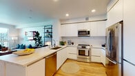 Located at 3333 S La Cienega Blvd in Los Angeles, CA, this modern single-floor residence offers a thoughtfully designed layout with clean architectural lines and contemporary finishes throughout. The open-concept kitchen is a standout feature, showcasing floor-to-ceiling white cabinetry, a marble-style tile backsplash, stainless steel appliances including a range, built-in microwave, dishwasher, and refrigerator, complemented by a generous island with bar seating — ideal for both cooking and casual dining. Light hardwood flooring flows seamlessly through the kitchen and into the connected living and dining areas. The living room is bright and inviting, anchored by large floor-to-ceiling windows that flood the space with natural light and offer open views of the surrounding Los Angeles cityscape. A private balcony extends the living space outdoors. The bedroom is generously proportioned with large windows providing additional natural light and urban views, and is complemented by a spacious walk-in closet with ample hanging and storage space. The bathroom features a sleek floating vanity with a wide mirror, clean tilework, and a refined, minimalist aesthetic. Recessed lighting throughout enhances the modern ambiance of this well-appointed Los Angeles residence.