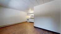 Located at 46 West St in Akron, Ohio, this single-floor unit offers a straightforward and functional layout across several distinct areas. The main living area features rich hardwood-style flooring and neutral-toned walls, providing a clean and versatile space. Adjacent to the living area, the kitchen is equipped with white cabinetry, a white range, and an under-cabinet range hood, all set against matching neutral walls and continued hardwood-style flooring.

The bedrooms are carpeted in warm beige tones and feature baseboard heating, offering a comfortable environment. One bedroom includes a large window dressed with blinds that invites natural light and exterior greenery views, while another features a window-unit air conditioner for additional climate control. Both bedrooms are served by closets — one with bi-fold doors and a hanging rod, and another with a single door and built-in shelving, providing ample storage.

The bathroom is cleanly appointed with a white vanity and sink, a mirrored medicine cabinet, tiled shower-tub surround, and continued hardwood-style flooring. Baseboard heating is present throughout the unit, ensuring consistent warmth. The overall layout is compact yet well-organized, making efficient use of the available space.