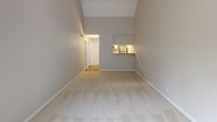 This 1-bedroom, 1-bathroom residence offers a thoughtfully laid-out single-floor plan with standout architectural details throughout. The living area immediately impresses with its dramatic vaulted ceilings accented by white-painted exposed wood beams and a tongue-and-groove ceiling, creating an airy, open atmosphere. Soft carpeting throughout the living and bedroom spaces adds warmth underfoot, while neutral gray walls provide a clean, versatile backdrop. A pass-through window connects the living area to the kitchen, enhancing the sense of openness between spaces. The kitchen features white cabinetry with brushed nickel hardware, laminate countertops, a stainless steel sink, and wood-look tile flooring, and is equipped with black appliances including a refrigerator, dishwasher, and range. The bedroom benefits from abundant natural light streaming through a sliding glass door that opens to a private balcony, offering pleasant outdoor views. The vaulted ceiling continues into the bedroom, reinforcing the spacious feel. A generously sized walk-in closet with wire shelving provides ample storage. The bathroom includes a full soaking tub and shower combination with chrome fixtures. A hallway with carpeted flooring and clean white doors connects the rooms, completing this well-appointed residence.