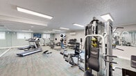 Located at 600 Valley Rd in Warrington, PA, this fitness center offers a thoughtfully designed space for comprehensive workouts across a single floor. The facility is accessed through a welcoming entryway adorned with soft blue patterned wallpaper, large-scale wall art, and a coat hook station, setting an inviting tone before entering the main workout area.

The main exercise floor features durable, multi-toned carpet flooring and is illuminated by recessed fluorescent lighting panels throughout. Full-length mirrored walls run along multiple sections of the space, amplifying the sense of openness and allowing users to monitor their form during exercise. A wall-mounted split HVAC unit ensures year-round climate control.

The cardio section is well-stocked with treadmills, elliptical trainers, and a stationary bike, including equipment from recognized brands such as Precor. The strength training area includes a multi-station cable machine, adjustable benches, and a comprehensive free weight rack with dumbbells of varying sizes. A dedicated functional training zone features a medicine ball tower, TRX resistance bands, exercise mats, and stability balls. Mounted flat-screen televisions provide entertainment throughout.

Natural light filters in through windows and a glass entry door, offering views of the surrounding outdoor greenery and contributing to an energizing workout environment.