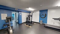 Located at 360 Main Street in Hartford, Connecticut, the 360 Fitness Center is a focused, single-floor fitness facility designed to deliver a comprehensive workout experience in an efficient, organized space. The interior features a clean, modern aesthetic with a bold blue and white color scheme that carries throughout, lending the gym an energetic and motivating atmosphere.

The facility is divided into two connected workout zones. The cardio area is equipped with a treadmill, elliptical trainer, and rowing machine, accompanied by a wall-mounted flat-screen television for entertainment during workouts. Frosted glass entry doors provide a polished, professional entrance to this section.

The strength training area is thoughtfully outfitted with a multi-functional cable machine, a power tower for bodyweight exercises, a full rack of dumbbells with an adjustable weight bench, and resistance bands mounted on the wall for functional training. Medicine balls on a dedicated rack round out the free weight offerings. Full-length mirrors along one wall support proper form and technique.

Motivational wall graphics, including a bold "Strength Comes From Within" mural and directional chevron artwork, reinforce the gym's energizing identity. Durable rubber flooring runs throughout, and overhead fluorescent lighting ensures the space is well-lit. The textured ceiling and structured layout give the center a practical, no-frills character suited for serious training.