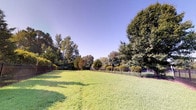 Located at 111 Cheswick Circle in Yorktown, Virginia, this single-story property offers a thoughtfully designed layout complemented by appealing indoor and outdoor features. The exterior showcases a generously sized, well-manicured lawn enclosed by a classic wrought iron fence, providing both security and an open, park-like atmosphere. Mature trees of varying species frame the perimeter, offering natural shade and privacy beneath clear blue skies. The landscaping is lush and carefully maintained, creating a serene outdoor environment.

The interior entry area sets a welcoming tone with warm, neutral-toned walls and earthy slate-style tile flooring that adds texture and durability underfoot. Large glass doors allow natural light to flow freely into the entry corridor, creating a bright and airy transition between the outdoors and interior spaces. Nautical-themed artwork adorns the walls, nodding to the area's coastal Virginia heritage. The entry also features practical safety elements, including a fire alarm pull station, and provides clear access to adjoining interior rooms. A glimpse through the glass doors reveals a spacious, light-filled interior room with ceiling fans and additional tile flooring, suggesting comfortable, functional living spaces beyond the entry.